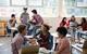 Photo of a classroom with some students sitting at their desks and others standing.