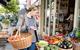 Young woman standing on street outside food shop looking at fresh produce on stall.